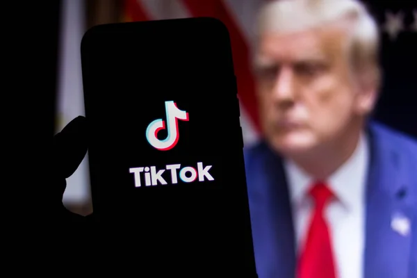 Explore TikTok's impact on social media with Donald Trump in the background, highlighting the intersection of politics and viral content. TikTok app on a smartphone screen with Donald Trump in the background, symbolizing the intersection of social media and politics.